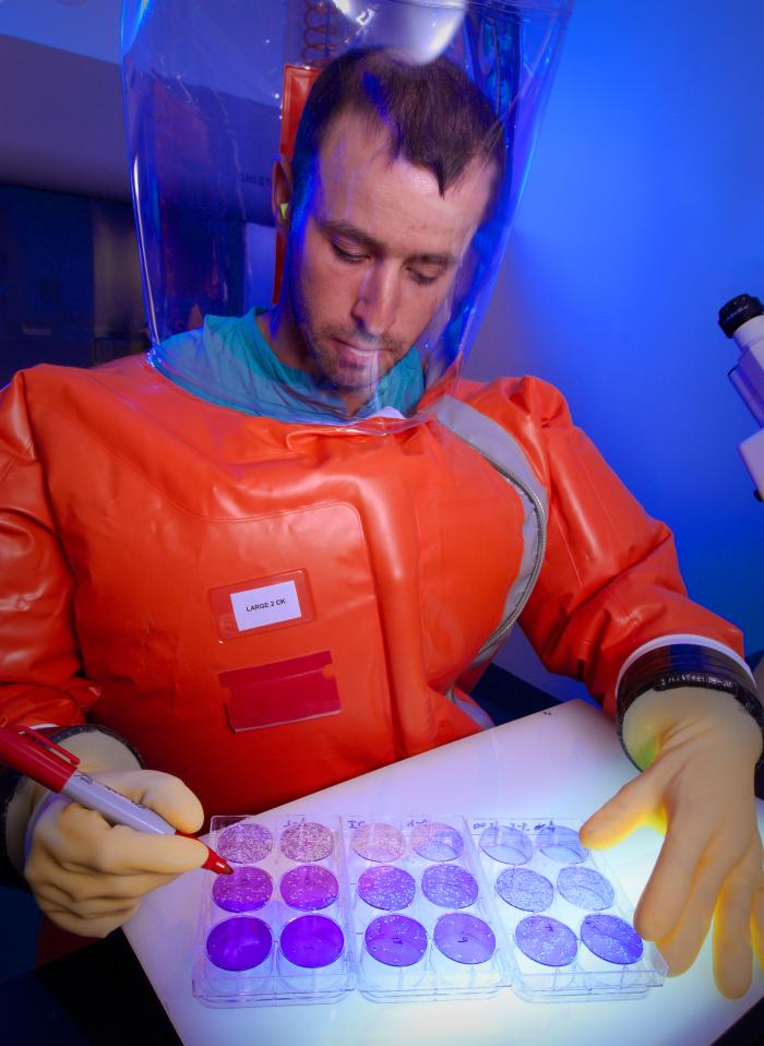 Centers for Disease Control microbiologist, and Special Pathogens Branch (SPB) staff member, as he was in the process of counting viral plaques within fixed monolayers of cells, set atop a light box. From Public Health Image Library (PHIL). [1]
